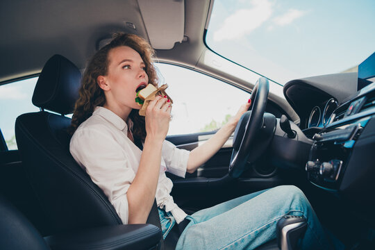 Photo of cheerful pretty lady dressed white shirt smiling driving rented automobile eating snack outdoors urban city street