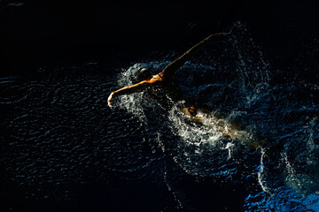 Female athlete swims with a butterfly style. Splashes of water scatter in different directions