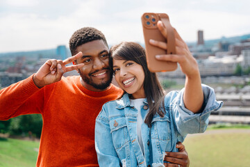Naklejka premium A Joyful Couple Takes a Selfie on a Sunny Day in the City Park Surrounded by Greenery
