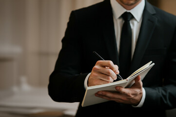 Hand of a man in a suit writing with a pen on a notebook
