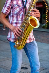 Obraz premium A talented street musician passionately plays the saxophone, captivating passersby with his soulful performance. The golden saxophone gleams in the sunlight, adding a touch of brilliance to the scene.