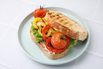 Tasty sandwich with grilled vegetables and cream cheese on white tiled table, closeup