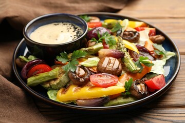 Delicious salad with grilled vegetables and sauce on wooden table, closeup