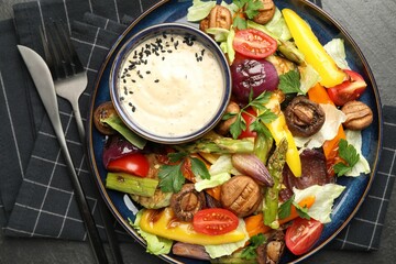 Delicious salad with grilled vegetables and sauce served on dark gray textured table, flat lay