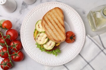 Tasty sandwich with grilled vegetables, fresh tomato and oil on white marble table, flat lay