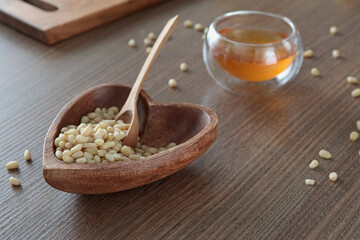 Natural pine nuts in heart shape bowl. Wooden dishes and furniture in kitchen. Fresh clear honey in glass bowl. Healthy products. 