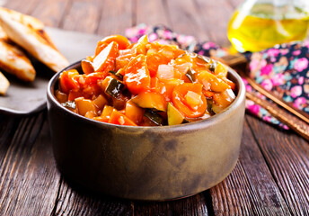 Summer Vegetable spicy stew of zucchini, potatoes, peppers, onions, tomatoes and eggplant in a bowl on the table.
