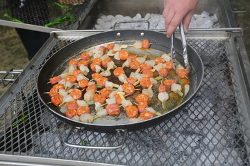 Chorizo and scallop skewers being cooked over charcoal outdoors