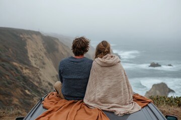 Fototapeta premium A couple, wrapped in a blanket, gazes at the vast ocean from the roof of their car positioned near cliffs, embodying peace, love, and appreciation for the serene coastal beauty.