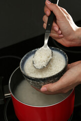 Woman taking boiled rice from pot into bowl, closeup