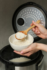 Woman taking boiled rice into bowl on grey background, closeup