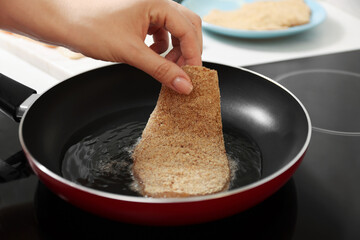Woman cooking schnitzel in frying pan on stove, closeup