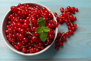 Fresh red currants in bowl and mint on light blue wooden table, top view