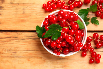 Fresh red currants and green leaves on wooden table, top view. Space for text