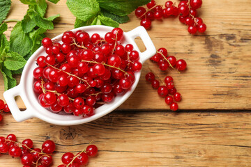 Fresh red currants in bowl and mint on wooden table, flat lay. Space for text