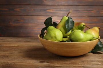 Fresh green pears and leaves in bowl on wooden table. Space for text