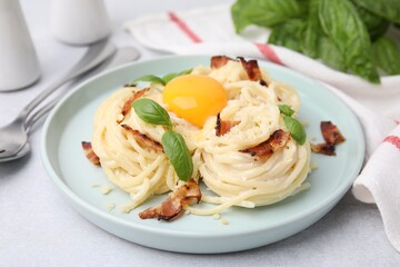 Delicious pasta Carbonara with egg yolk, bacon and basil on light gray table, closeup