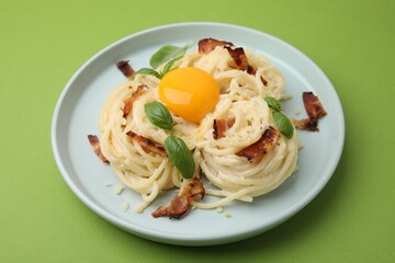 Delicious pasta Carbonara with egg yolk, bacon and basil on green table, closeup