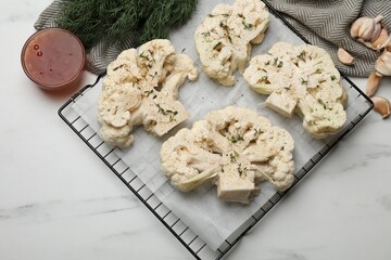 Uncooked cauliflower steaks, dill, garlic and sauce on white marble table, top view