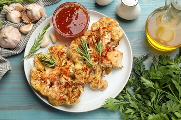 Delicious baked cauliflower steaks with sauce served on blue wooden table, flat lay