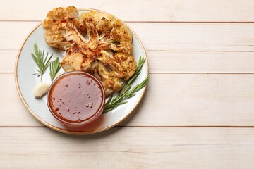 Delicious baked cauliflower steaks with sauce, garlic and rosemary on wooden table, top view. Space for text