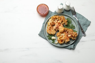 Delicious baked cauliflower steaks with garlic and parsley on white table, flat lay. Space for text