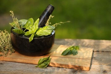 Fresh herbs. Basil leaves in mortar and thyme on wooden table outdoors, closeup. Space for text