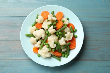 Tasty cooked cauliflower with green peas, string beans and carrot slices on light blue wooden table, top view