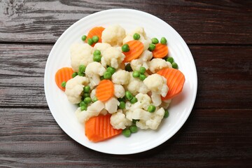 Tasty cooked cauliflower with green peas and carrot slices on wooden table, top view
