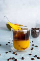 A glass of iced coffee with mango juice and coffee beans on a table