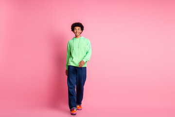 Fototapeta premium Full size photo of nice young man walk empty space ad wear green hoodie isolated on pink color background
