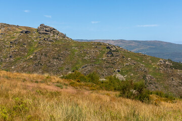 Northern Portuguese landscape in the Portuguese district of Braga near the town of Fafe with granite boulders, green mountains and hills and a blue sky.