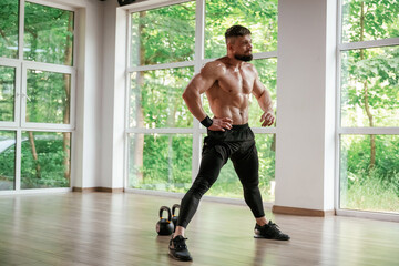 Daytime, trees outside the windows. Strong muscular man is working out in the gym