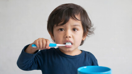 Adorable child brushing teeth with blue toothbrush. Daily hygiene, health habits. Bright simple background. Morning routine for dental care. Ideal for dental health awareness, parenting tips.
