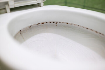 Dirt under the rim of toilet bowl. Close up view of dirty canals from which water flows in the...
