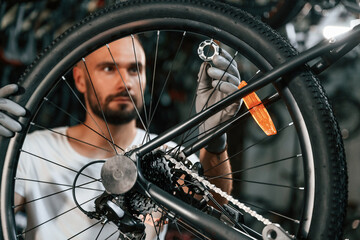 Spokes replacement. Repair man in bicycle shop, working in store