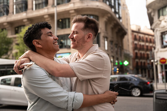 Multiethnic gay couple laughing and embracing in the city