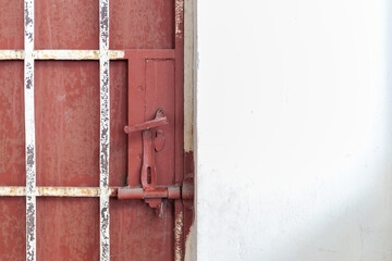 A close-up of a rusty red door with a latch, contrasting against a white wall. Ideal for themes of confinement and isolation.