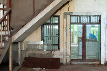Abandoned interior space showcasing vintage architecture, worn walls, and rustic metal elements under a staircase.