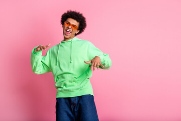 Portrait of cool young man dance empty space wear green hoodie isolated on pink color background