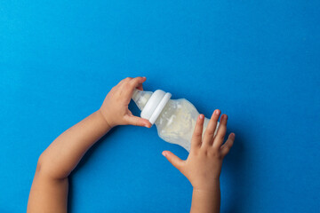 A toddler Reaching For milk feeding bottle, against blue back ground, top shot