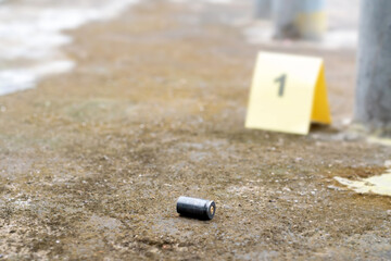 Evidence regarding firearms, Pistol bullet shell on cement floor with blurred number one on yellow...