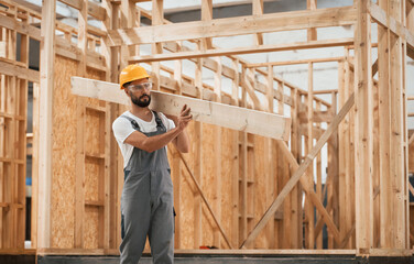 Fototapeta premium Walking, holding plank. Industrial worker in wooden warehouse