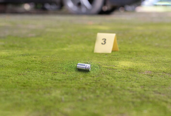 Pistol bullet shell and blurred number 3 on yellow paper on cement floor which has bright green...