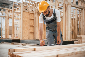 Standing, marking plank by pencil. Industrial worker in wooden warehouse