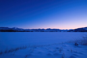 Fototapeta premium A serene winter landscape at dusk with snow-covered ground and mountains in the background.