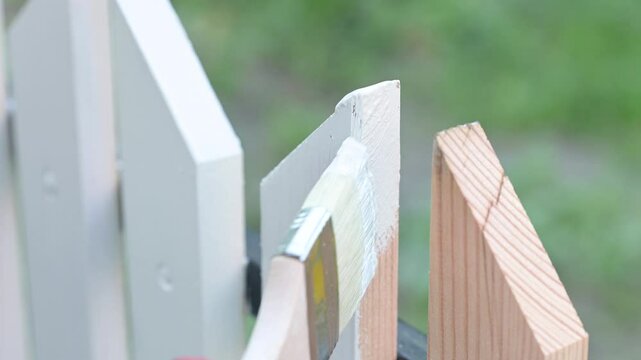 Painting wooden fence in white color. Motion of hand with paintbrush carefully painting wooden plank of fence