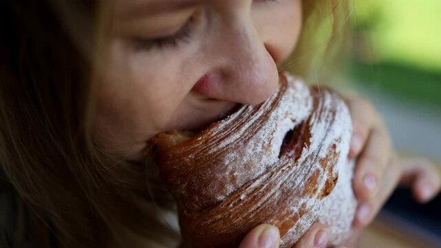 A close-up of a girl taking an appetizing bite of a croissant and chewing. Top view. Croissant breakfast.