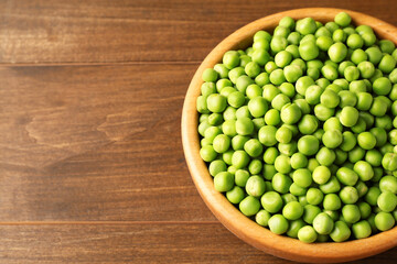 Fresh green peas in bowl on wooden table. Space for text
