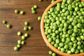 Fresh green peas in bowl on wooden table, above view. Space for text